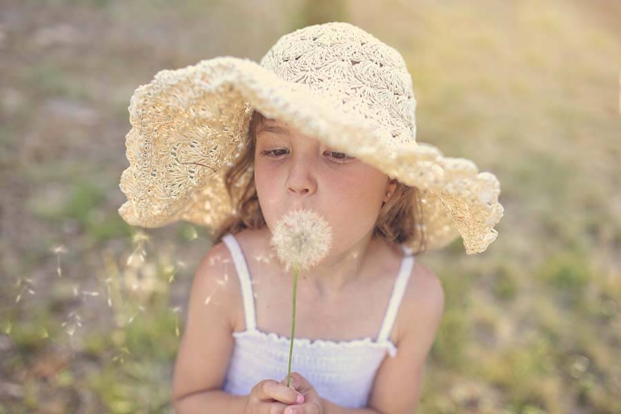 young girl blowing seeds from flower
